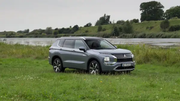 Szary Mitsubishi Outlander PHEV zaparkowany na łące nad jeziorem.