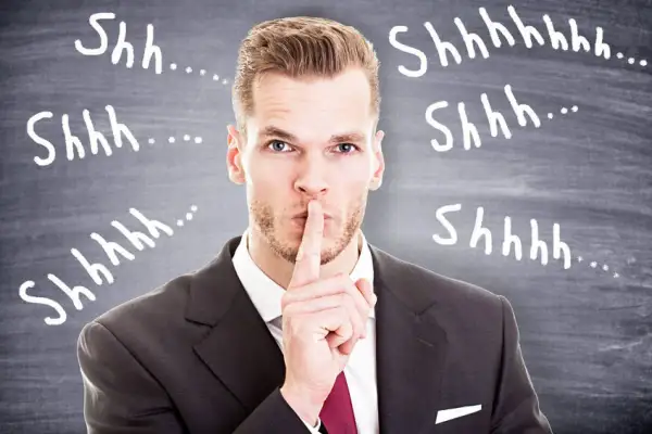 Uomo d'affari con dito sulle labbra, circondato da "Shhh..." scritti sulla lavagna. Il silenzio assenso significato è chiaro: non parlare.