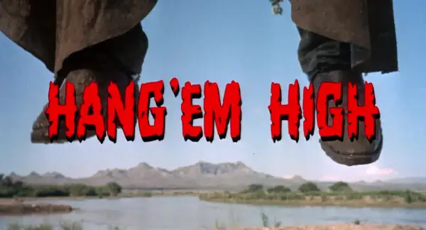 Nogi w kowbojkach wiszą nad rzeką. Czerwony napis "HANG 'EM HIGH" sugeruje westernowe porachunki.