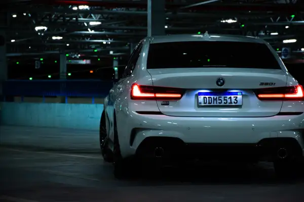 Vue arrière d'une BMW blanche dans un parking sombre. L'éclairage de la plaque d'immatriculation est bien visible, soulignant son caractère obligatoire.