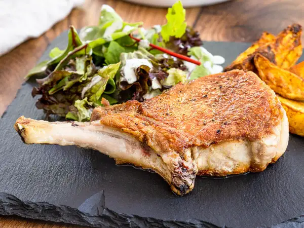 Saftiges Kotelett im Backofen, goldbraun gebraten, serviert mit knusprigen Kartoffelspalten und frischem Salat.