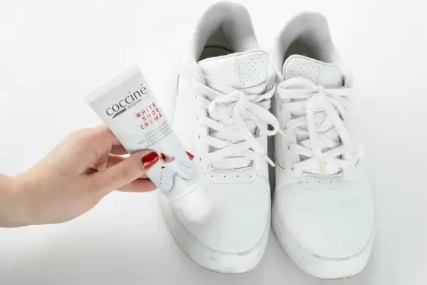 Mano con tubetto di crema per scarpe bianche, pronto a pulire le sneakers. Un metodo efficace per far tornare come nuove le tue scarpe bianche.