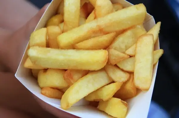 Złociste, grube frytki belgijskie w papierowym rożku.