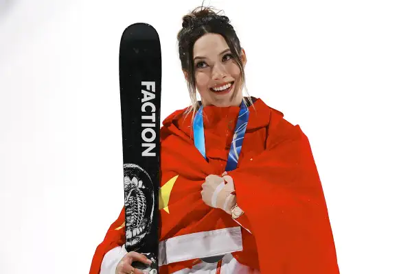 Eileen Gu, sonriente y envuelta en la bandera china, sostiene un esquí Faction.