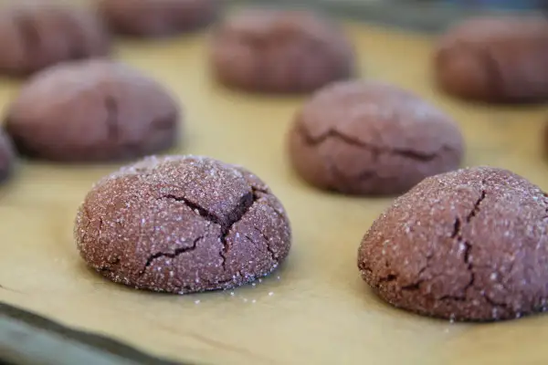 Mörka, sprickiga nutella kakor täckta med socker ligger på ett bakplåtspapper.