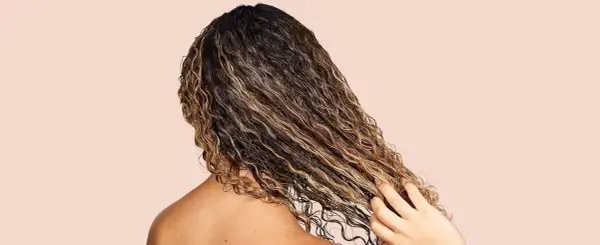 Cabello rizado y húmedo con reflejos dorados, mostrando cómo fortalecer el pelo con productos nutritivos.
