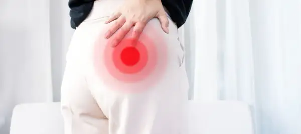 Person håller handen mot höften där en röd cirkel indikerar smärta, möjligen relaterad till piriformis triggerpunkt.