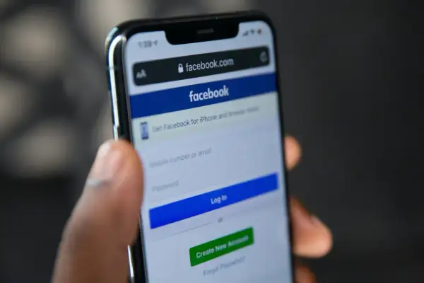 Dłoń trzyma smartfon z ekranem logowania Facebooka. Szukasz sposobu, jak odzyskać konto na FB bez maila i telefonu?