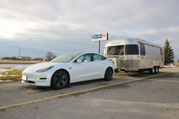 Une voiture électrique blanche tracte une caravane Airstream argentée. La question "peut on tracter avec une voiture electrique" trouve ici une réponse visuelle.