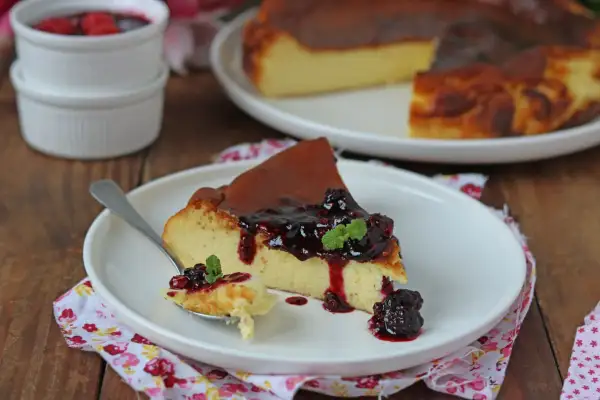 Una fetta di cheesecake basca cremosa, con topping di frutti di bosco e menta, su un piatto bianco.