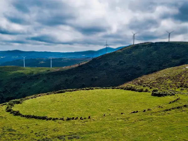 Prado das Chantas, un paisaje verde con molinos de viento en colinas onduladas bajo un cielo nublado.