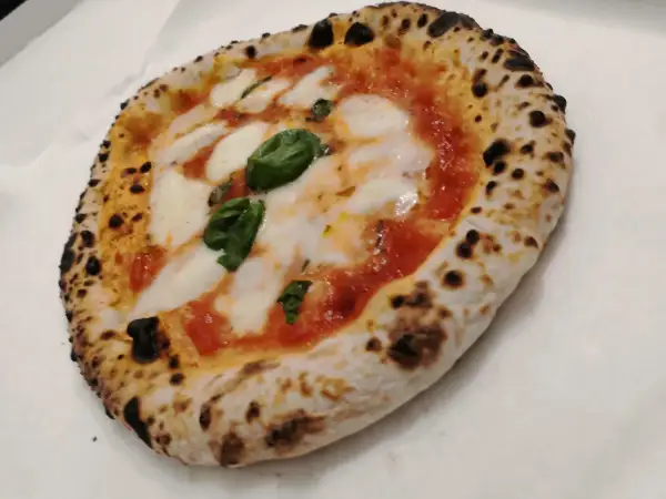 Une authentique pizza napolitaine, avec sa croûte gonflée et légèrement brûlée, garnie de sauce tomate, de mozzarella fondante et de feuilles de basilic frais.