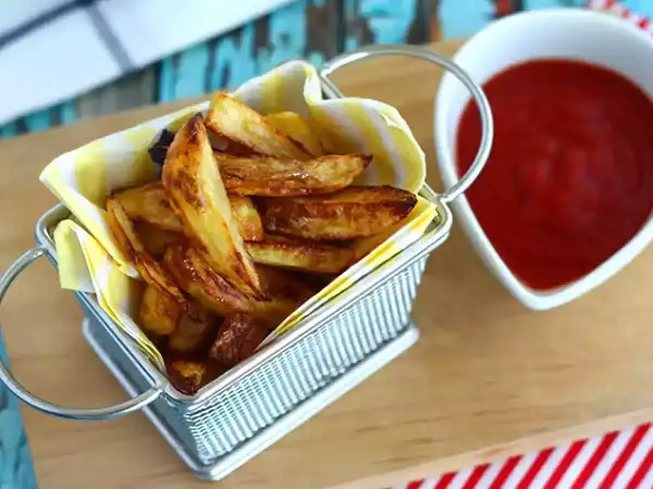 Un panier rempli de délicieuses frites au four dorées, à côté d'un bol de ketchup rouge vif.