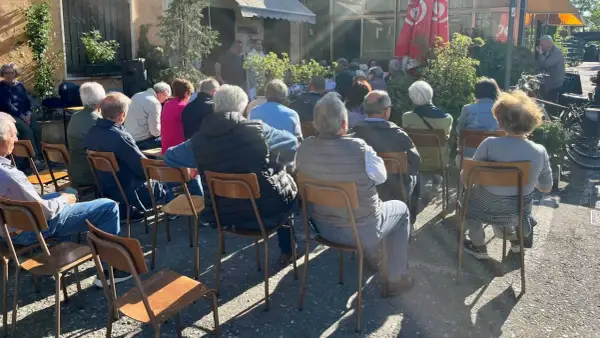 Un gruppo di persone ascolta un relatore durante un tricot cafè tutorial all'aperto.