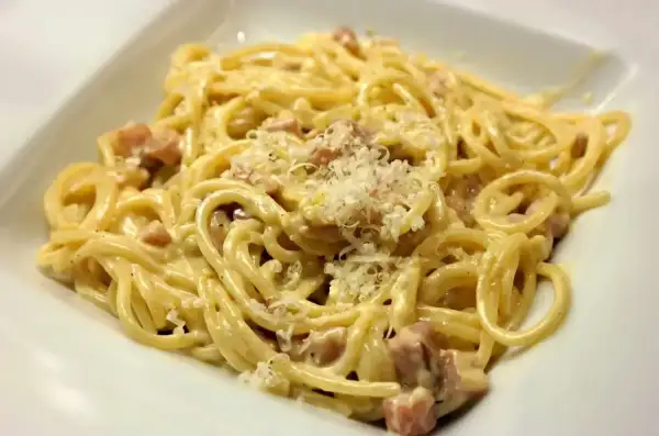 Pyszne spaghetti carbonara ze śmietaną 30, posypane parmezanem i kawałkami boczku.