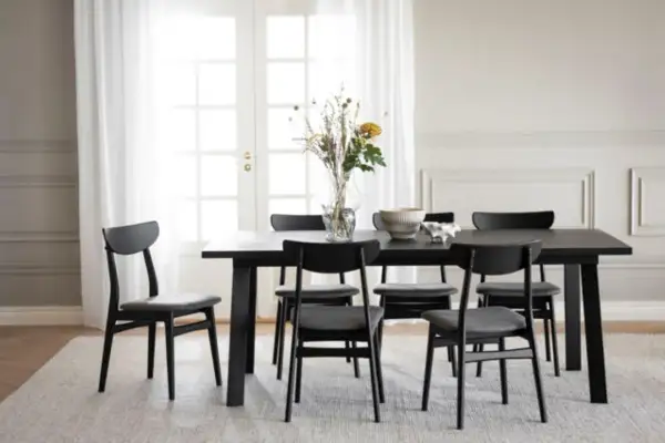 Ett modernt matbord med sex svarta stolar. Utrymme runt matbordet är inrett med en vas med blommor och en skål.