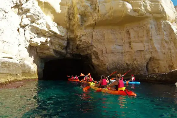 Kayakistas exploran las impresionantes cuevas de Cabo de Gata, navegando por aguas cristalinas bajo acantilados dorados.