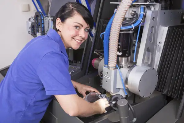 Frau mit blauen Polohemd arbeitet an einer CNC-Maschine. Sie vertieft sich in ihre Weiterbildung als Zerspanungsmechanikerin.