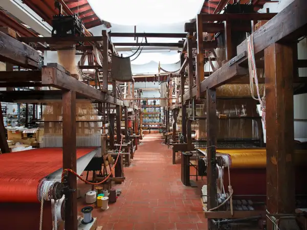 Interno di un antico setificio fiorentino con telai in legno e tessuti colorati.