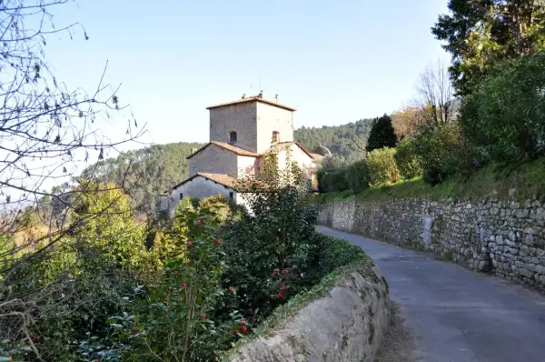 Strada panoramica verso Sant'Andrea di Compito, con un antico borgo in pietra e vegetazione rigogliosa.