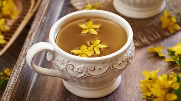 Aromaticzna herbata z dziurawca w ozdobnej filiżance, pływające żółte kwiaty dodają uroku.