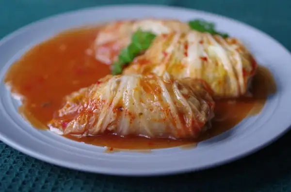 Pyszne gołąbki z kapusty pekińskiej w sosie pomidorowym, udekorowane natką pietruszki.