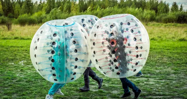 Tre personer i genomskinliga bubblor, redo för bumperball hyra. En rolig utomhusaktivitet med mycket skratt.