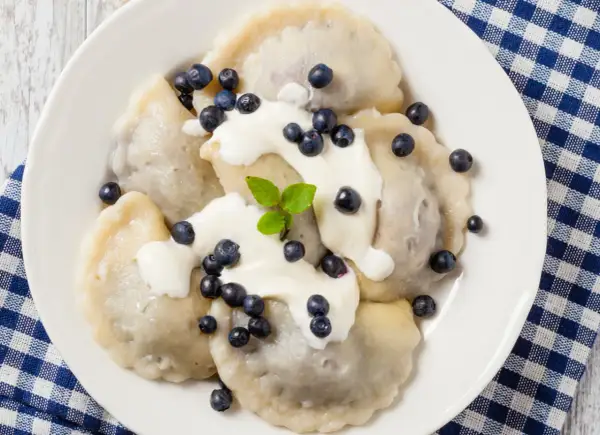 Pyszne pierogi z jagodami, polane śmietaną i posypane świeżymi owocami. Idealne na letni deser.