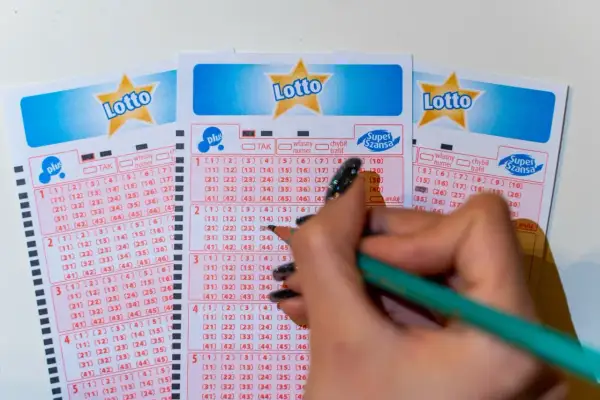 Ręka z ołówkiem zaznacza liczby na kuponach Lotto. Poznaj, jakimi metodami można zawierać zakłady gier liczbowych, wybierając swoje szczęśliwe cyfry.