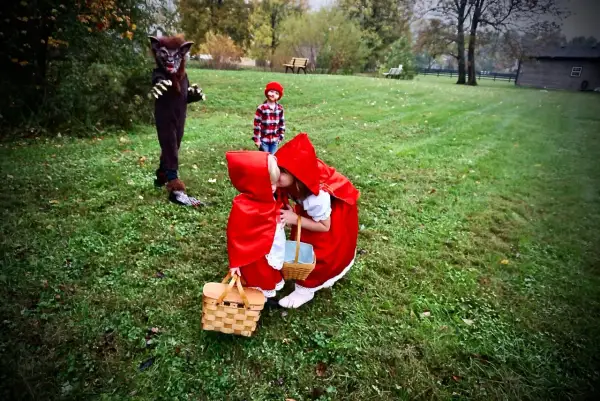 Dzieci w strojach Czerwonego Kapturka i wilk na trawiastym podwórku.