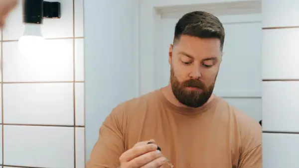 Visage homme 50 ans, barbe rousse, tenant un compte-gouttes.