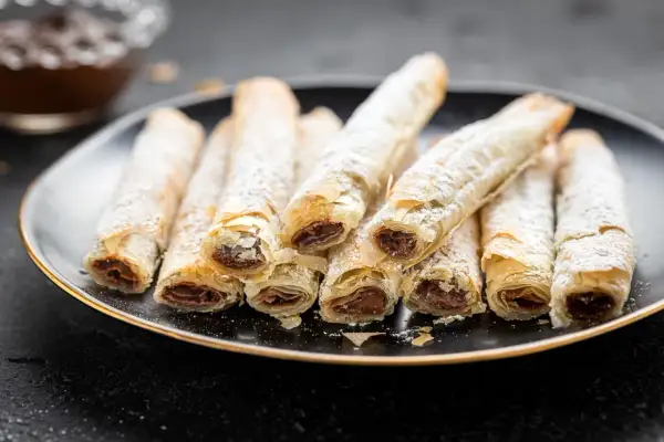Rotolini croccanti di pasta fillo ripieni di cioccolato, spolverati di zucchero a velo.