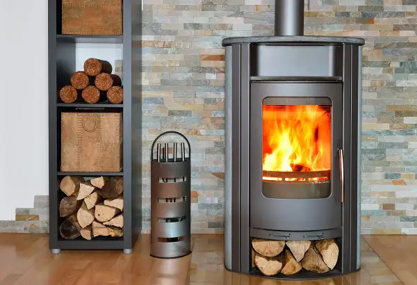 Un poêle à bois crépitant, avec du bois rangé à côté. Un accessoire pour le feu est présent.