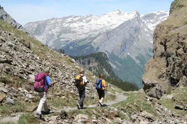Trois randonneurs se baladent sur un sentier rocailleux, admirant les montagnes enneigées et les vallées verdoyantes.