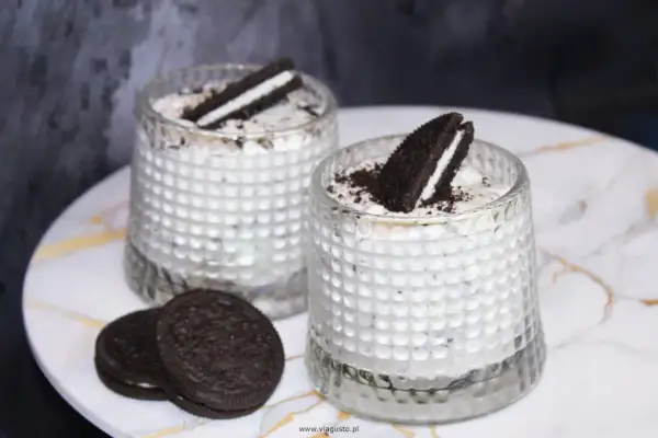 Dwa deserki z kremem i pokruszonymi oreo ciastkami, ozdobione połówkami ciastek.