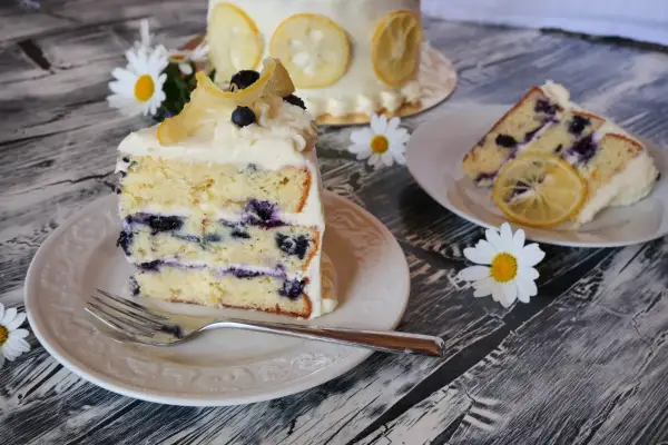Ein Stück saftiger Zitronen-Blaubeerkuchen mit cremigem Frosting, garniert mit kandierten Zitronenscheiben und frischen Blaubeeren.