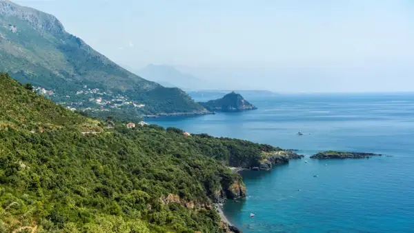 Costa verde e blu intenso del policastro mare, con case sparse tra la vegetazione e montagne sullo sfondo.