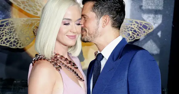 Orlando Bloom szepcze coś do ucha Katy Perry, która uśmiecha się z zamkniętymi oczami.