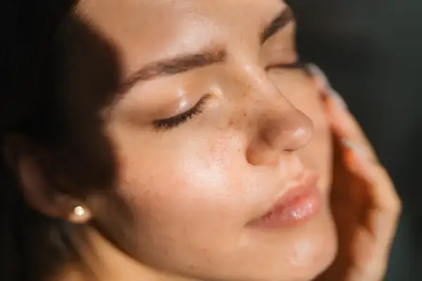 Viso di donna con lentiggini, illuminato da luce soffusa. La pelle appare curata, suggerendo che retinolo e vitamina C si possono usare insieme per un incarnato radioso.