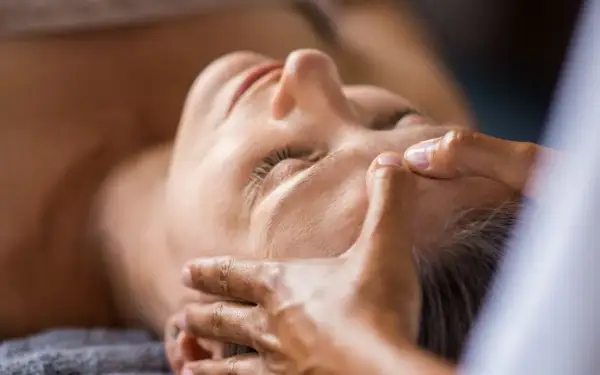 Mani esperte dimostrano come massaggiare il viso per le rughe, con un tocco delicato sulla fronte e sulle tempie per un effetto rilassante e ringiovanente.