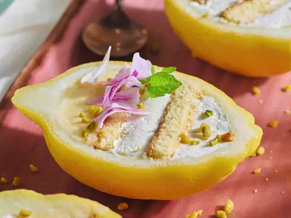 Delizia al limone: crema soffice e biscotti in un limone scavato, guarnito con pistacchi e petali rosa.
