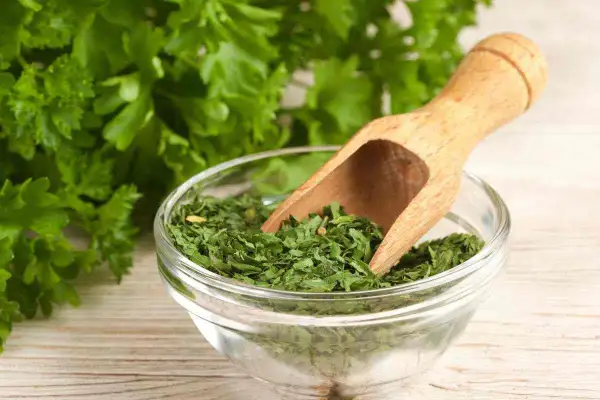 Prezzemolo essiccato in una ciotola di vetro, con un mestolo di legno. Un'erba aromatica utile anche in gravidanza.