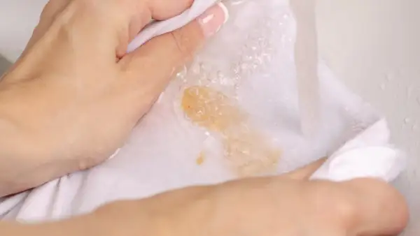 Hände waschen ein weißes Tuch mit Kaffeeflecken unter fließendem Wasser. So lassen sich Kaffeeflecken entfernen.