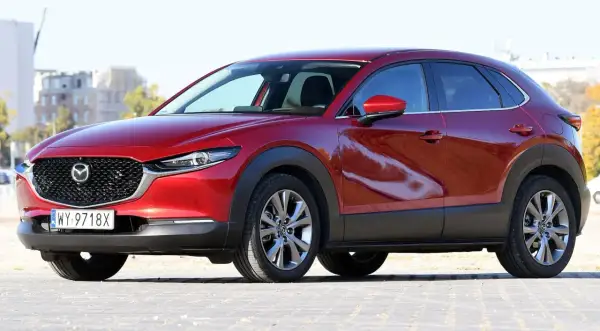 Czerwona Mazda CX-30 z polskimi tablicami rejestracyjnymi stoi na zewnątrz.