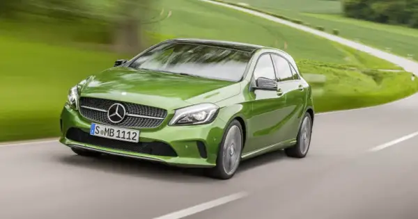 Zielony Mercedes klasy C pędzi po krętej drodze wśród zielonych pól.