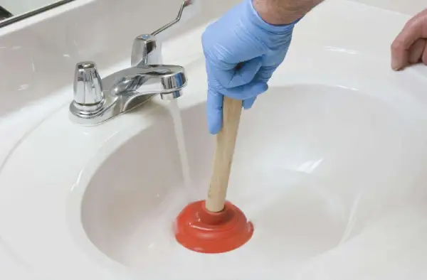 Main tenant utilise une ventouse pour déboucher un lavabo. L'eau s'accumule, signe d'un lavabo bouché.