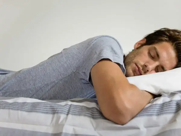 Hombre durmiendo boca abajo, con la cabeza apoyada en una almohada. Se pregunta: "porque sudo mucho cuando duermo soy hombre".