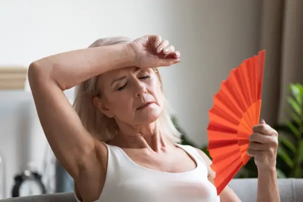 Frau fächelt sich mit einem orangefarbenen Fächer Luft zu, um etwas gegen Hitzewallungen zu tun.