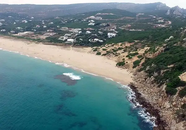 Vista aérea de la playa de los alemanes en Foz, con casas blancas dispersas entre la vegetación y el mar turquesa.