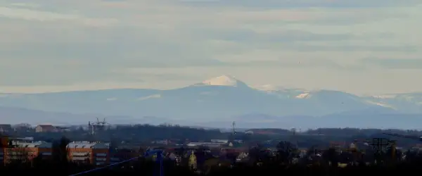 Widok na Śnieżkę i Karkonosze z Wrocławia. W oddali majaczą ośnieżone szczyty górskie, a na pierwszym planie widać zabudowania miejskie.